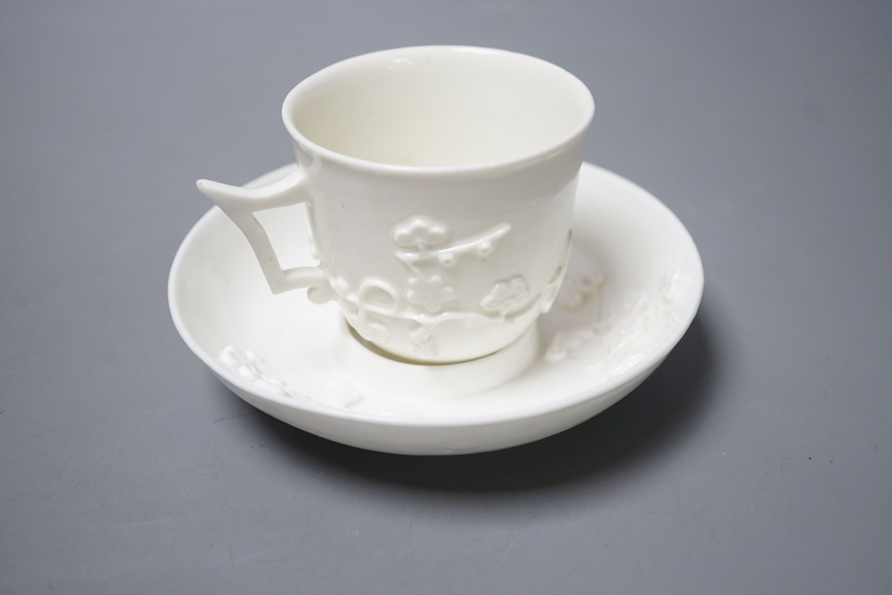 A St Cloud white-glazed coffee cup with angular handle and scroll terminal and matching trembleuse saucer applied with sprigs of flowering prunus c. 1730